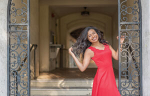 A high school senior girl wearing a red dress is posing for Khim Higgins Photography in Winter Park, Florida.