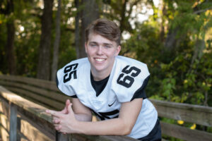 A high school senior boy wearing a football jersey is leaning over a rail.