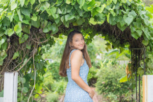senior girl wearing a blue dress is standing under a canopy of greenery at Leu Gardens