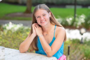 Lake Mary senior girl in a blue tank top and pink skirt is leaning on a white pillar table and smiling at Khim Higgins Photography.