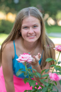 Lake mary senior photo session with Jen who is wearing a blue tank top and pink skirt. Jen is posing in front of some pink roses.