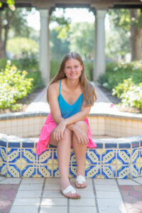 Lake Mary senior girl in a blue tank top and pink skirt is sitting on a fountain ledge.