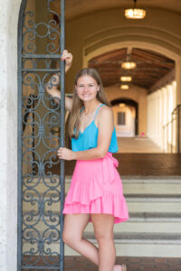 Lake mary senior photo shoot with Jen wearing a blue tank top and pink skirt and she is leaning agains black iron gate.