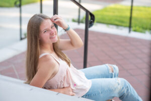 Lake Mary senior photo shoot with a senior girl in a pink sleeveless top with blue jeans and she is sitting on a set of stairs and leaning back on her right arm.