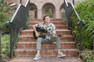 A high school senior boy is playing with his car sitting on stairs while Khim Higgins Photography takes his photos.