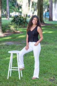 A lake mary senior girl standing in the middle of a park near a white stool with one foot on the stool.