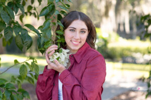 A senior girl wearing a long sleeve maroon shirt is holding white flowers in her hands.