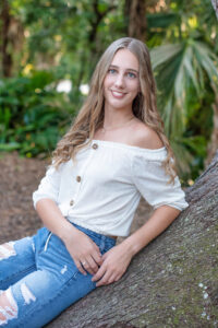 Oviedo High School Senior, Alina is wearing a white shirt with jeans and she is leaning on a tree as Orlando senior photographer, Khim Higgins photograph her.