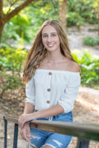 Oviedo High School senior Alina is wearing a white off the shoulder shirt with jeans. She is standing and leaning on a rail as Orlando senior photographer takes her photo.