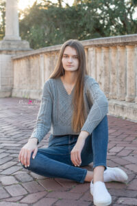 Lake Mary senior portrait session of a girl in jeans and long sleeve gray shirt is siting on a bridge.