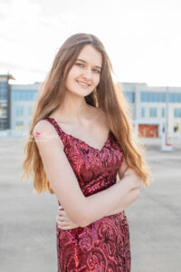 Lake mary high school senior photo shoot with Ella who is wearing a long red sequence prom dress with her arms wrapped around her waist standing on the top floor of a parking garage.