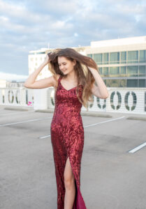 A lake mary senior girl in a long red sequence dress is walking on the top floor of a garage.