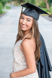 Senior girl from Oviedo High School is wearing her graduation cap and holding her gown behind her shoulder.