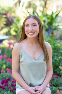 OHS senior photo shoot at Meade Gardens with Sara. Sara is wearing a sage color top and white shorts and she is sitting on a log looking at Khim Higgins Photography.