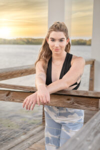 OHS senior shoot with Khim Higgins Photography with Mary who is wearing a black top and jeans. Mary is standing by a lake leaning on wooden rails.