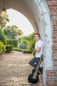 Orlando senior boy photo shoot leaning on the wall with his guitar next to his leg and his arms are crossed in front of him.