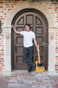 Orlando senior boy photo shoot with his guitar by a decorative brown door.