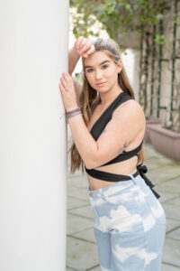 Oviedo High School senior girl, Mary is wearing a black top and blue jeans. She is leaning on a white pole looking at Khim Higgins Photography's camera.