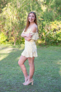 senior girl in a yellow dress has her arm crossed in front and looking to the side over her left shoulder at Orlando senior photographer.