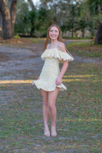 senior girl in a yellow dress is twirling side to side as Khim higgins photographer snaps her photo.