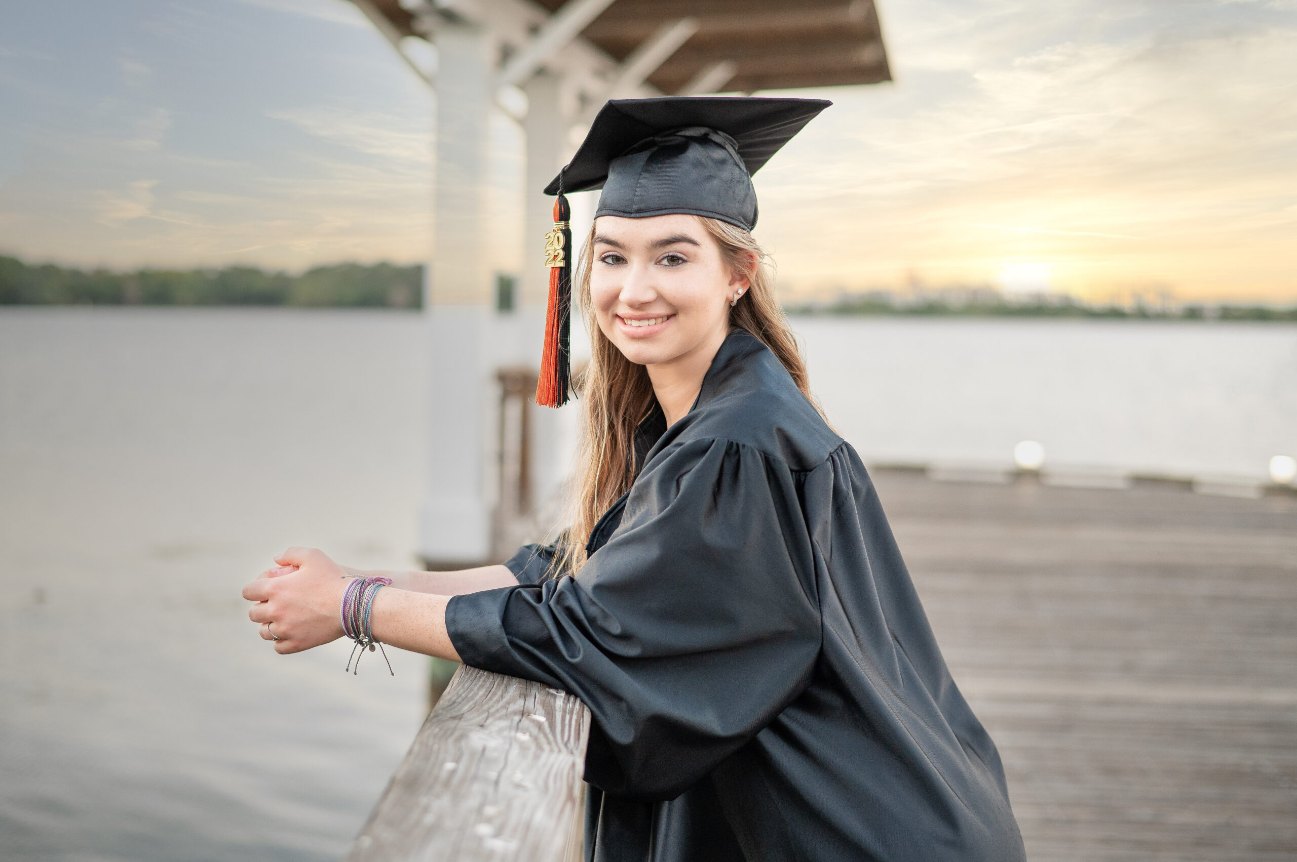 Oviedo High School senior, Mary is wearing her cap and gown and standing by a lake smiling at Orlando senior photographer, Khim Higgins