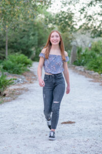 senior girl from OHS is wearing a purple top with black jeans is walking and smiling at Khim Higgins Photography.