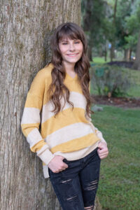 Timber Creek senior girl is standing and leaning against a tree smiling at Orlando Senior Photographer.