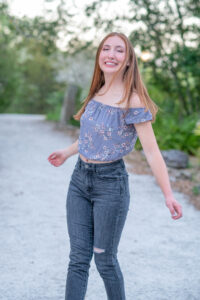 senior girl from oviedo high school is in a purple top and black jeans is twirling around as Khim Higgins Photography snaps her picture.