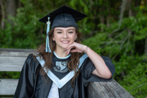 Kailey is a senior at Hagerty High School and she is wearing her graduation cap and gown and sitting on a bench for Khim Higgins Photography to take her picture.