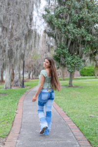 A senior girl from Oviedo High School is walking away from the camera and looking over her shoulder as she smiles at Orlando Senior Photographer.