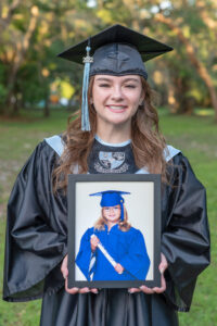 Hagerty High School senior is wearing her cap and gown and she is holding a framed baby picture of her when she was in kindergarten. 