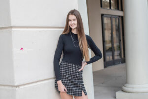 Lake mary senior portait session with a senior girl wearing a long black sleeve shirt and black checkered skirt is leaning on a wall.