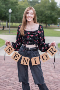 A senior girl from Oviedo is wearing a blue shirt with black pants smiling at Khim Higgins Photography.