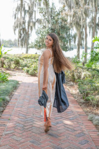 A senior girl from Oviedo is holding her cap and gown as she walks away and turns and looks over her shoulder at Orlando Senior Photographer.