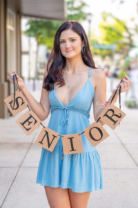 Winter Park High School senior girl is in a blue dress and she is holding a 'senior' banner as Orlando senior photographer takes her picture.