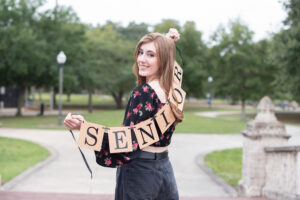 A Lake Mary high school senior girl is holding a banner sign that says "senior" and looking over her left shoulder.