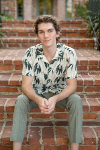 Orlando senior boy photoshoot with the model wearing a floral beigh and green button up shirt and green pants sitting on a set of stairs 