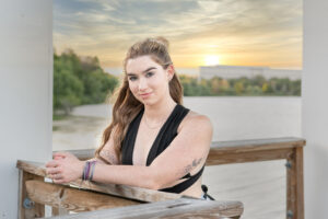 Mary, a beautiful senior girl from OHS is leaning on a wooden rail by the lake.