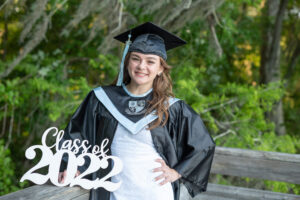 HHS senior is wearing her cap and gown holding a class of 2022 sign smiling as Khim Higgins Photography takes her picture.