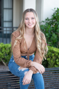 A beautiful long blond hair senior girl from Hagerty High School is sitting on a bench looking at Orlando Senior Photographer as she gets her picture taken.