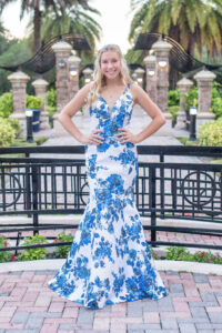 Lake Mary senior girl photo shoot with Khim Higgins Photography. Senior girl is in her blue and white prom dress standing with both hands on her hips smiling at Khim Higgins Photography.