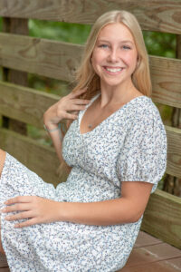 Lake Mary High School Senior Shoot with a blond senior girl wearing a blue dress and she is sitting on a dock smiling at the photographer Khim Higgins.