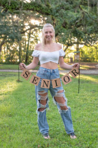 Senior girl photos shoot from lake mary high school who is wearing a white shirt and jeans, holding a SENIOR banner.