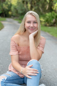 Senior girl from Lake Mary high school is sitting in the middle of a road smiling at photographer Khim Higgins.