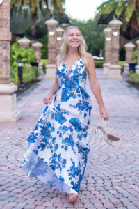 Senior girl in a blue and white dress is walking towards Orlando Senior Photographer while holding her shoes.