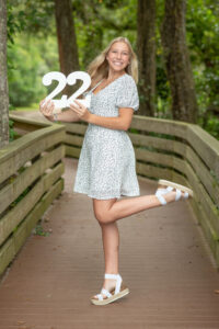 Lake Mary Senior Photo Shoot with a senior girl wearing a blue dress and holding a '22' sign smiling at Khim Higgins Photography.