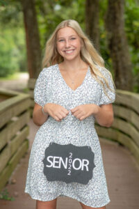 Senior girl photo shoot of a Lake Mary High School student with Khim Higgins Photography. The senior girl is in a blue dress and she is holding a sign that says 'senior.'