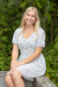 Senior girl from Lake Mary High School is wearing a blue dress sitting on a wooden rail smiling at Khim Higgins Photography.