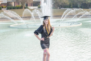 A UCF graduate standing in the Reflection Pond wearing her cap.