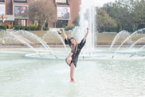 ucf grad standing in the reflection pond holding a bottle of champagne